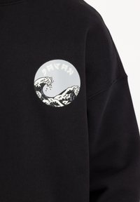 Felpa nera con un grafico circolare sul petto, che raffigura onde in bianco e nero su uno sfondo grigio chiaro.