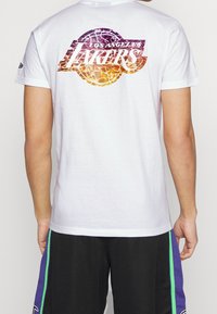 Vit bomull T-shirt med en livfull lila och orange Los Angeles Lakers grafik på baksidan, med en slät yta och korta ärmar.