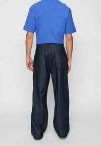 Mörkblå denim byxor med vida ben och en lätt textur. Har bakfickor med sömdetaljer. Matchas med en blå kortärmad skjorta.