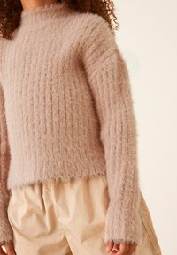 Rosa fluffig tröja med hög hals, ribbat mönster och lätt fransade kanter, i kombination med ljusbeiga shorts.