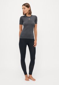 Grå t-skjorte med kort erm laget av et mykt materiale, paret med svarte, tettsittende leggings med teksturerte detaljer ved anklene.