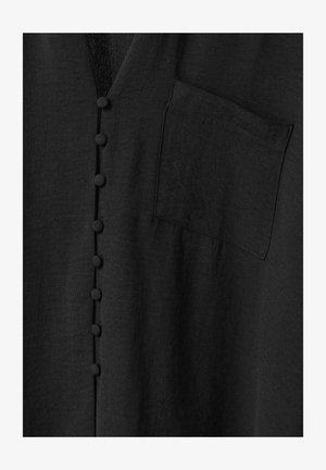 Vêtement noir en tissu texturé, avec un col en V, cinq boutons en tissu et une poche plaquée unique sur le côté gauche.