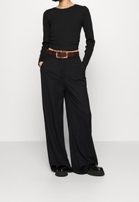 Černý dlouhý rukáv crop top spárovaný se širokými černými kalhotami. Hnědý opasek s texturovanou, vzorovanou sponou. Černé boty na robustní podrážce.