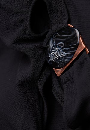 Must mustriga mustreeritud pind, kus on väljapaistv kaarjas must kivi, millel on sinised ja valged veerised, raamis vaskhardware.