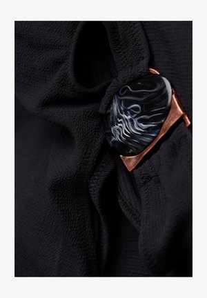 Fekete, textúrált felületű szövet, amelyen egy kiemelkedő, ívelt fekete kő található kék és fehér örvényekkel, réz keretezéssel.