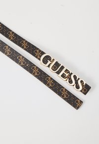 Juodas dirbtinės odos diržas su auksiniu "GUESS" logotipu ir kartojančiuosius rudo atspalvio logotipo raštu, tekstūruota paviršius su detaliu siuvimu.