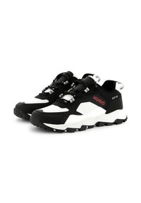 Scarpe sportive in bianco e nero con tomaia testurizzata, suola in gomma sagomata e hardware riflettente. Logo sul lato in rosso.