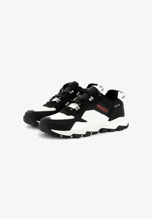 Scarpe sportive in bianco e nero con tomaia testurizzata, suola in gomma sagomata e hardware riflettente. Logo sul lato in rosso.