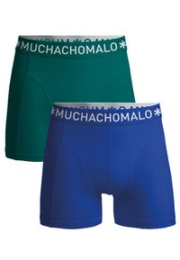 Dve pare moških bokseric v zeleni in modri barvi, narejene iz zračnega materiala. Vsaka ima bel, blagovno znamko označen pas z napisom "MUCHACHO".