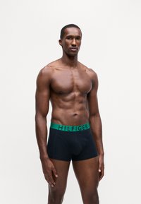 Boxeri negri cu o mână de elastic verde inscripționat cu "HILFIGER". Țesătura pare netedă și oferă un design ajustat.