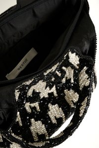 Sac à main en perles noir et blanc avec un motif texturé, fermeture éclair, et intérieur en tissu noir. L'étiquette indique "GESTUZ."