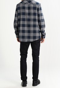 Flanellen overhemd in grijs en marineblauw ruitpatroon, lange mouwen, relaxed fit, gecombineerd met zwarte broek en zwarte schoenen, achteraanzicht.