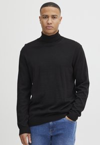 Zwarte coltrui gemaakt van zachte gebreide stof, met lange mouwen en geribbelde manchetten. Gecombineerd met blauwe denim jeans.