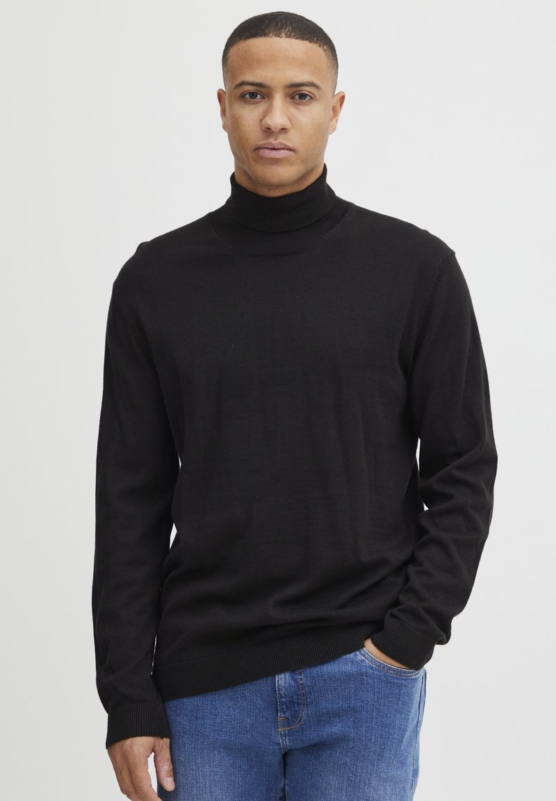 Zwarte coltrui gemaakt van zachte gebreide stof, met lange mouwen en geribbelde manchetten. Gecombineerd met blauwe denim jeans.