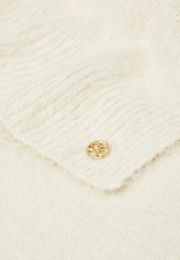 Crèmekleurige gebreide trui met een gestructureerde weving en een gouden knoopdetail. De stof lijkt zacht en iets pluizig te zijn.