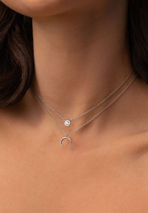 Silberne geschichtete Halsketten mit einem runden Kristallanhänger und einem mondförmigen Charme, vor nackter Haut.