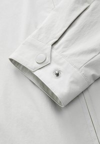 Lichtgrijze overhemdmanchet met een gladde textuur, voorzien van een ronde knoop en een drukknoopsluiting, benadrukt door contrasterende stikdetails.