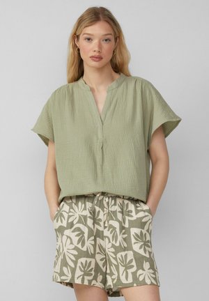 Olive green short-sleeved top with a V-neck and textured fabric, paired with beige shorts featuring a green foliage pattern.