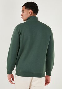 Sweatshirt verde con collo alto e polsini elasticizzati. Realizzato in materiale morbido, presenta un design semplice e una vestibilità comoda.