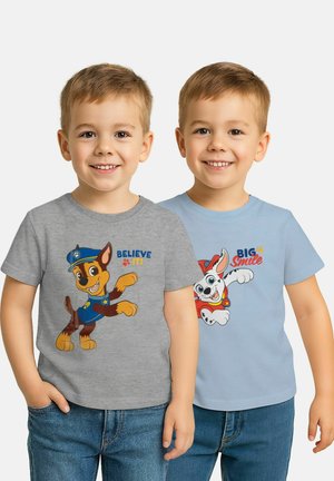 Two smiling boys wearing jeans and Paw Patrol t-shirts, one gray with "Believe It!" and one light blue with "Big Smile" text.