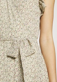 Kukallinen kietaisumekko vaaleanbeigestä kankaasta, jossa pienet vaaleanpunaiset ja vihreät kuviot, kerätty vyötärö ja solmittu rusetti.