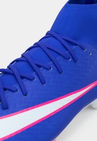 Μπλε ποδοσφαιρικό παπούτσι με υφασμένη επιφάνεια, με μοβ κορδόνια και λευκή ρίγα με ροζ λεπτομέρειες. Σχεδιασμένο για απόδοση και πρόσφυση.