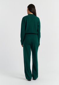 Groene gebreide twee-delige outfit, met een relaxte sweater en wijde broek, gladde textuur en subtiele stikdetails.