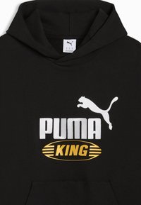 Sweat à capuche noir avec logo Puma blanc au-dessus d'un ovale doré contenant le mot "KING", montrant la partie supérieure avant et la capuche.
