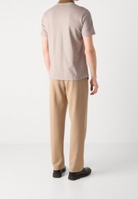 T-shirt beige à manches courtes avec un col contrastant, associé à un pantalon beige et des chaussures noires. Design simple et coupe ajustée.