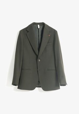 Blazer de un solo botón en verde oscuro, con solapas de muesca, bolsillos de ojal en la parte delantera y un pequeño pin redondo en la solapa izquierda.