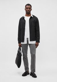 Veste noire à boutons, chemise rayée blanche, pantalon gris, chaussures noires et sac fourre-tout noir. Design moderne et simple, tissu léger.