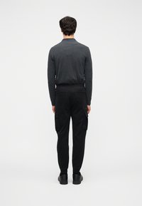 Μαύροι παντελόνες cargo με πλαϊνές τσέπες και ελαστικά τελειώματα, σε συνδυασμό με σκοτεινό γκρι μακρυμάνικο πάνω μέρος. Η εικόνα είναι από πίσω.