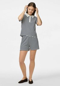 Námořnické a bílé pruhované polo tričko s krátkým rukávem, límečkem a zápínáním na knoflíky, spárované s odpovídajícími pruhovanými šortkami. Semišové nazouvací boty.