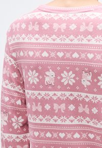 Różowy materiał z wzorem serc, kokardek i kształtów geometrycznych oraz drobnymi motywami jeleni w kolorze białym, tworzący miękkie, teksturowane wykończenie.