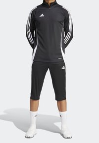 Top sportivo nero a manica lunga con zip e strisce laterali bianche, abbinato a pantaloni corti neri fino al ginocchio e calze bianche. Tessuto testurizzato.