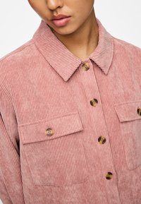 Roze corduroy overhemd met verticale ribbels, borstzakken en bruine knopen. Heeft een geknipte kraag en een relaxte pasvorm.