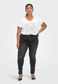 Witte V-hals T-shirt met zwarte handgeschreven tekst, gecombineerd met donkere skinny jeans en zwarte flats met een kettingaccent. Eenvoudig ontwerp, geen patronen.