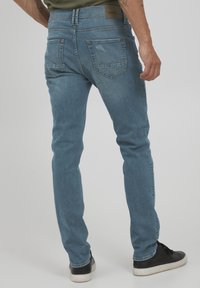 Vaqueros de mezclilla azul claro con un corte ajustado, con una cintura de altura media, bolsillos traseros clásicos y un sutil detalle de desgastado. Se llevan zapatos negros.