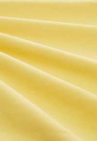 Gult tyg med en slät, texturerad yta, draperad i mjuka veck, som framhäver dess lätta och flexibla egenskaper.