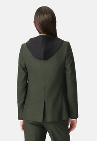 Giacca da uomo verde oliva con cappuccio nero, vestibilità slim, tessuto testurizzato e spacchetto singolo sul retro. Include tasche a pattina e spalle strutturate.