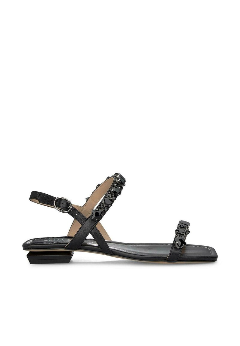 Sandalias planas negras con diseño de tiras, adornadas con gemas negras, que cuentan con un pequeño tacón cuadrado y hebilla ajustable en el tobillo. Textura suave.
