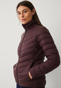 Giacca puffer bordeaux con design a cuciture verticali, colletto alto, chiusura con zip frontale e tasche laterali. Tessuto morbido e leggero.