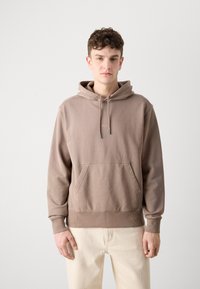 Beige hoodie gemaakt van zachte stof, met een voorzak, ribgebreide manchetten, verstelbare trekkoordkap en subtiele logo-details op de borst.