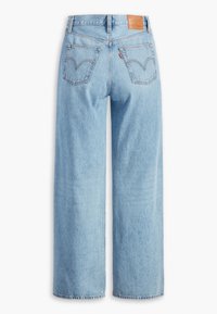 Jean bleu clair taille haute à jambe large avec deux poches arrière, un patch de marque en cuir marron et une petite étiquette rouge sur la poche droite.