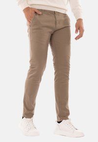 Chino in misto cotone beige con vestibilità slim e tasche laterali, abbinati a sneakers bianche. Texture liscia, dettagli di cucitura minimal.