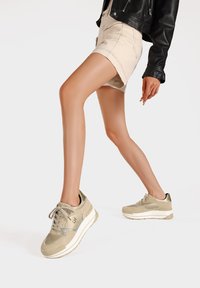 Sneakers beige chiaro con una finitura testurizzata, dotate di dettagli argentati, design con lacci e una suola spessa bianca.