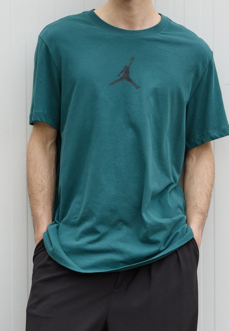 Teal bomullströja med korta ärmar och rund halsringning, med en svart Jumpman-logotyp på bröstet och en avslappnad passform.