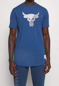Blauwe t-shirt van lichtgewicht stof met een zilveren stierlogo op de borst. Heeft korte mouwen en een ronde hals.