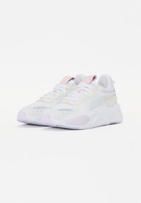 Witte sneakers met roze accenten, voorzien van een textuur bovenkant, mesh panelen en een robuuste witte zool. Veters en logo op de tong zijn zichtbaar.