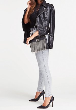Czarna skórzana kurtka motocyklowa na czarnym koronkowym topie, szare obcisłe dżinsy i czarne szpilki; kopertówka z frędzlami.